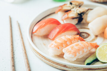 Set of sushi and maki on plate with soy sauce and chopsticks on white background. Top view with copy space