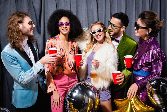 smiling interracial friends in sunglasses standing on grey background.