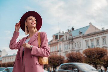 Outdoor portrait of elegant smiling woman wearing stylish pink blazer,  with yellow shoulder bag,...