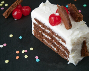 Black forest slice decorated with cherries, small pieces of cake and decorative and colorful sugar sprinkles on a black slate board. Close up View