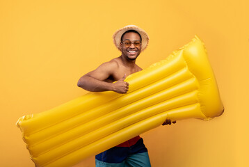 Summertime beach fun. Positive black man in swimsuit going to pool with inflatable lilo, showing...