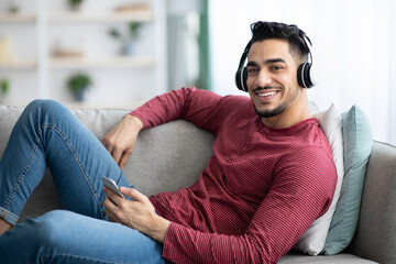 Obraz premium Cheerful arab guy listening to music, using mobile phone
