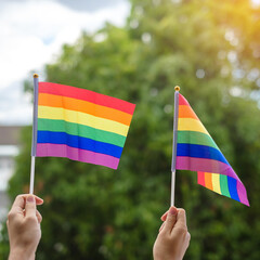 hands showing LGBTQ Rainbow flag on green nature background. Support Lesbian, Gay, Bisexual, Transgender and Queer community and Pride month concept