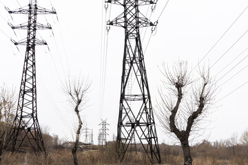 Electric city pole with gray sky and bare tree branches. High voltage pole.