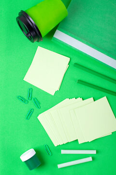 Stationery supplies and paper cup on green. Monochrome back to school flat lay