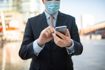 Masked businessman using his smartphone outdoor, covid and coronavirus concept