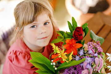 Naklejka na ściany i meble Little preschool girl with flower bouquet at home. Toddler child putting colorful garden summer flowers in small bottles with water. Home activities for kids. Flowers in rainbow colors. Happy child.