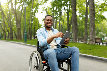 Portrait of cheeful impaired young man in wheelchair using laptop for remote communication at city park
