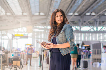 Asian business woman with passport and baggage checking flight information at airport and copy space area for your advertising looking away.