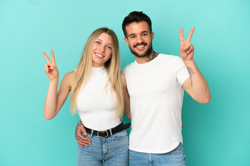 Young couple over isolated blue background smiling and showing victory sign