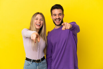 Young couple over isolated yellow background points finger to the front