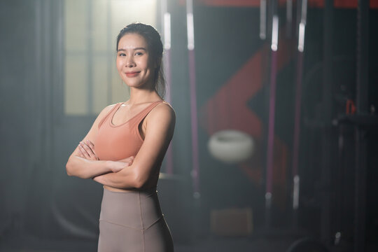 Selective focus at Asian women wearing sport cloth with smile inside of the gym before exercise and weight lifting inside fitness gym to workout for physical body strength and firm arms muscle