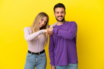 Young couple over isolated yellow background bumping fists