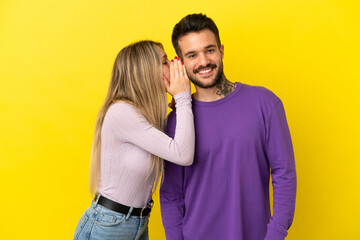 Obraz premium Young couple over isolated yellow background whispering something