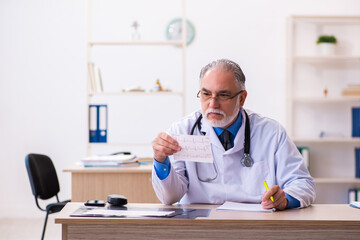 Old male doctor cardiologist looking electrocardiogram