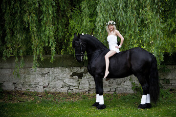 Blonde woman with white mystical dress on a black shire horse