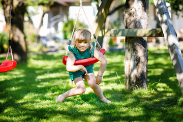 Happy little preschool girl having fun on swing in domestic garden. Healthy toddler child swinging on sunny summer day. Children activity outdoor, active smiling kid laughing - obrazy, fototapety, plakaty