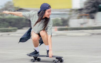 Beautiful happy Asian healthy woman smiling, motion speed riding and playing extreme sportive skateboard as outdoor activity with happiness, relaxation and fun during holidays in summer vacation. - obrazy, fototapety, plakaty