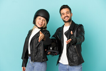 Couple with motorcycle helmet over isolated blue background shaking hands for closing a good deal
