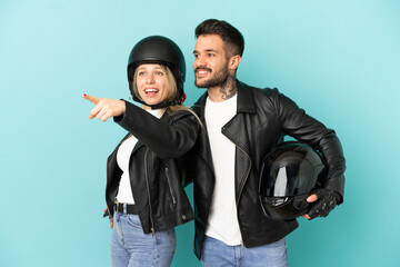 Couple with motorcycle helmet over isolated blue background pointing to the side to present a product