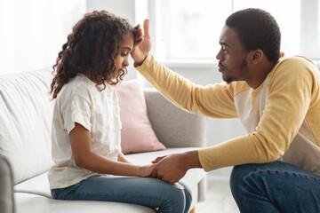 Black father touching his kid forehead, home interior