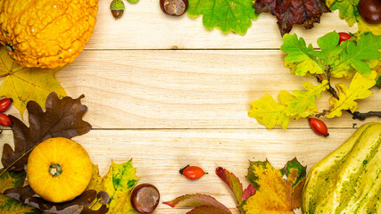 Abstract autumn. Natural harvest with orange pumpkin, fall dried leaves, red berries and acorns, chestnuts on wooden background in shape frame. Flat lay, top view, copy space.