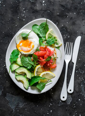 Delicious breakfast, brunch - poached egg, salmon, avocado, arugula salad on a dark background, top view