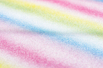 Background covered with glitter in diagonal lines in different colors of the rainbow, view from an angle.
