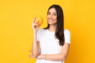 Young caucasian woman holding an orange over isolated yellow background