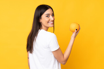 Young caucasian woman holding an orange over isolated yellow background