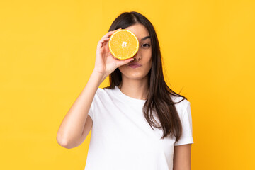 Young caucasian woman holding an orange over isolated yellow background