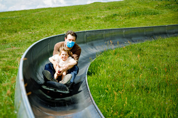 Little toddler girl and father having fun riding summer toboggan run sled down a hill. Active...