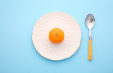 Clean spoon with plate and tangerine on color background