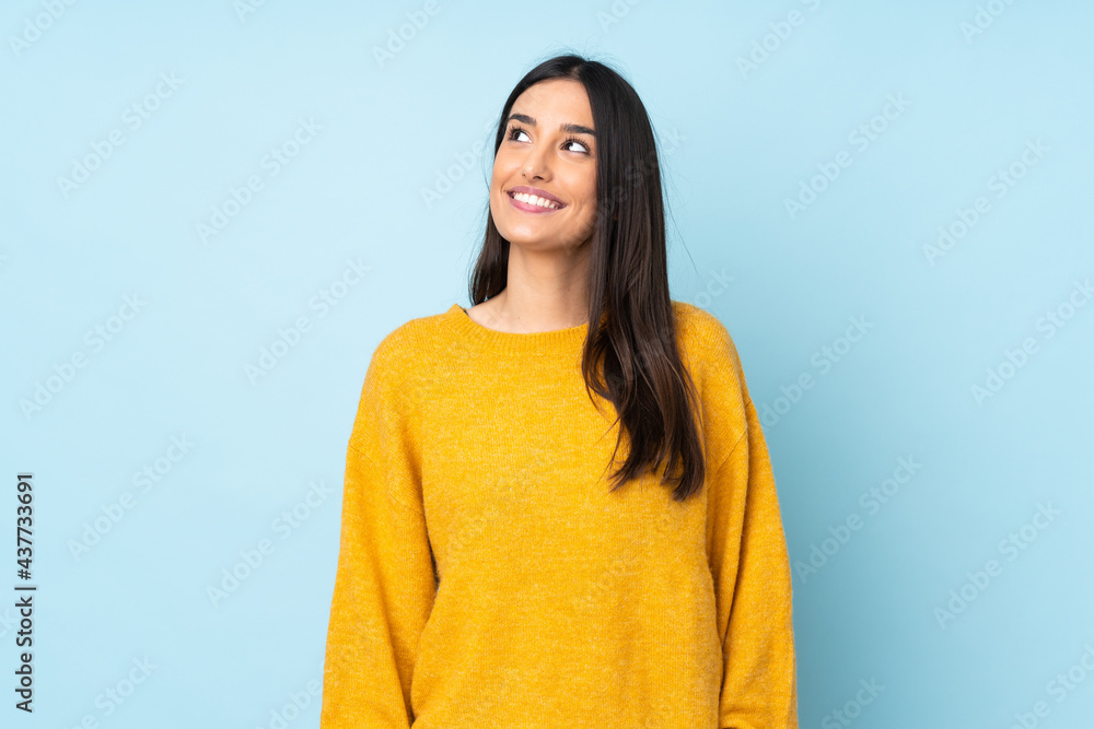 Wall mural Young caucasian woman isolated on blue background thinking an idea while looking up