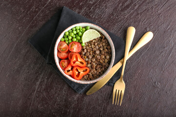 Bowl of tasty cooked lentils and vegetables on dark background