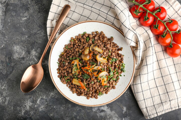 Plate with tasty cooked lentils and mushrooms on grunge background