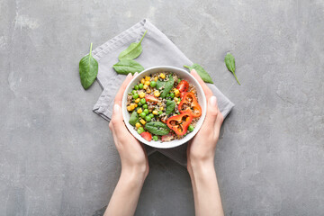 Female hands with healthy quinoa salad in bowl on grunge background