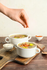 Woman seasoning tasty lentil soup in pot