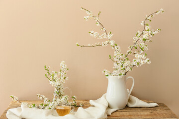 Cup with tasty tea and jug with blooming branches on wooden table