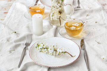 Table setting with blooming branches and cups of tea on light background