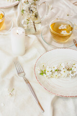 Table setting with blooming branches and cup of tea on light background
