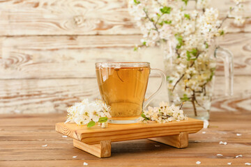 Cup with tasty tea and blooming branches on wooden background