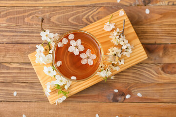 Cup with tasty tea and blooming branches on wooden background