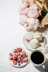 coffee, peonies and macaroons on white bed linen. Breakfast in bed. Scandinavian style. Flat lay, top view 
