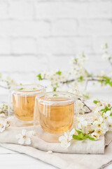 Glasses with tasty tea and blooming branches on light wooden background