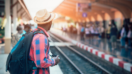 African male traveler waiting for the train on railway station. Adventure travel concept