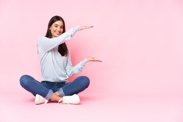 Young caucasian woman isolated on pink background holding copyspace to insert an ad