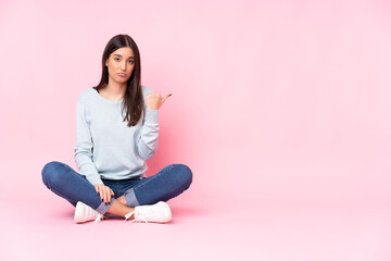 Young caucasian woman isolated on pink background unhappy and pointing to the side