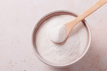 Collagen powder and spoon on beige stone background, top view