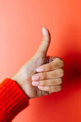 Woman's hand in red sweater shows thumb up, vertical frame on red background